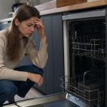 Femme inquiète agenouillée devant lave-vaisselle ouvert